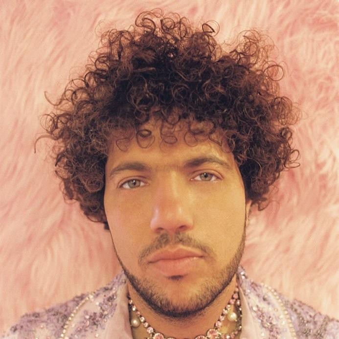 Benny Blanco w studiu nagraniowym, skupiony na pracy przy konsoli mikserskiej, otoczony sprzętem muzycznym.