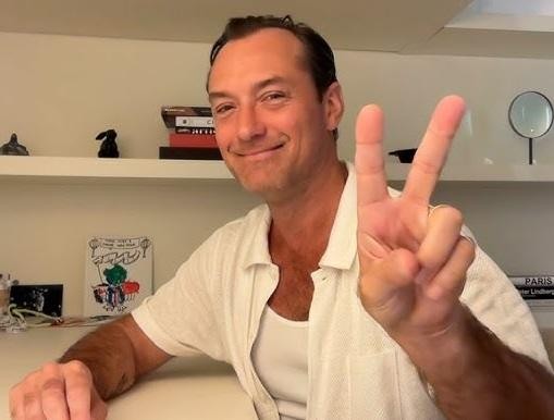Jude Law na scenie teatralnej, w dynamicznej pozie, oświetlony światłami reflektorów, symbolizujący jego osiągnięcia aktorskie.