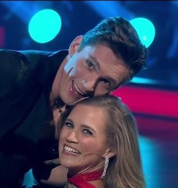 Agnieszka Kaczorowska w dynamicznej pozie tanecznej, prezentująca umiejętności w tańcu latynoamerykańskim, w eleganckim stroju tanecznym.