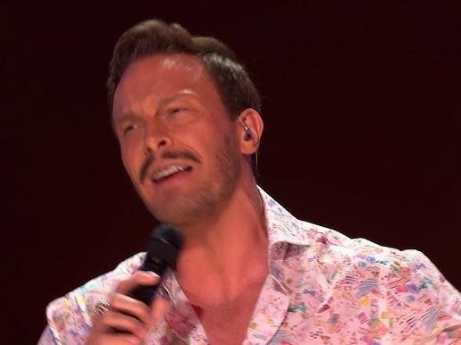 Sławek Uniatowski na scenie, śpiewający z pasją do mikrofonu, w tle widoczny instrument muzyczny, co oddaje jego wszechstronność i dynamikę występu.