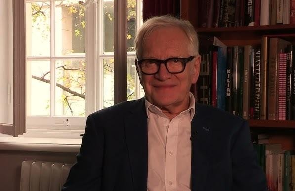 Andrzej Seweryn na scenie teatralnej, dynamicznie grający rolę, z teatralnym oświetleniem podkreślającym jego obecność.
