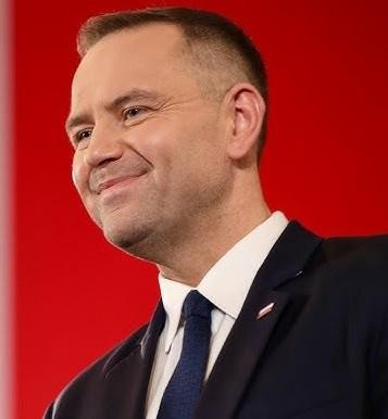 Karol Nawrocki w trakcie wystąpienia publicznego, na tle symbolizującym jego działalność historyczną i społeczną.