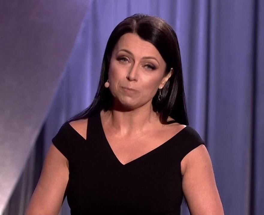 Adrianna Borek w trakcie występu kabaretowego, z ekspresyjną mimiką i gestykulacją, na scenie w świetle reflektorów.