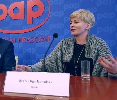 Beata Olga Kowalska na scenie teatralnej podczas występu, w dynamicznej pozie, z teatralnym oświetleniem i tłem.